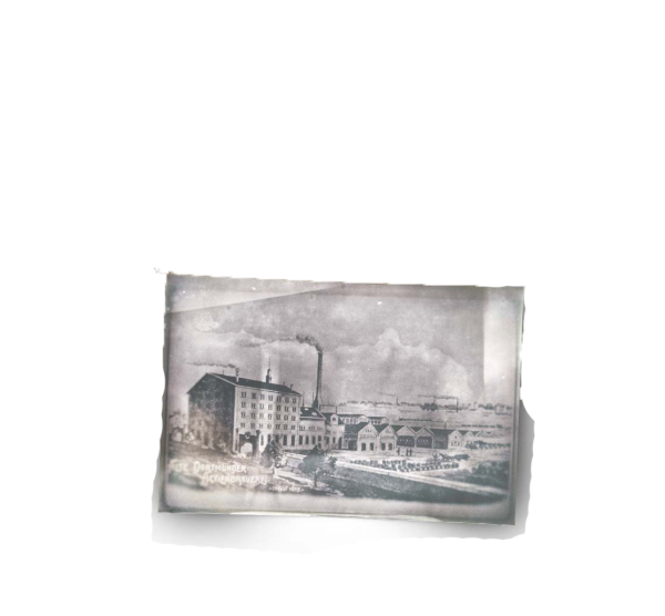 Altes Foto zeigt rauchende Schornsteine an einem Fabrikgelände neben einem Fluss.