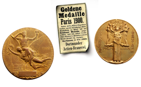 Zwei goldene Medaillen und ein Informationsblatt sind dargestellt. Eine Medaille zeigt eine Frau mit Stadtansicht, die andere drei Figuren.